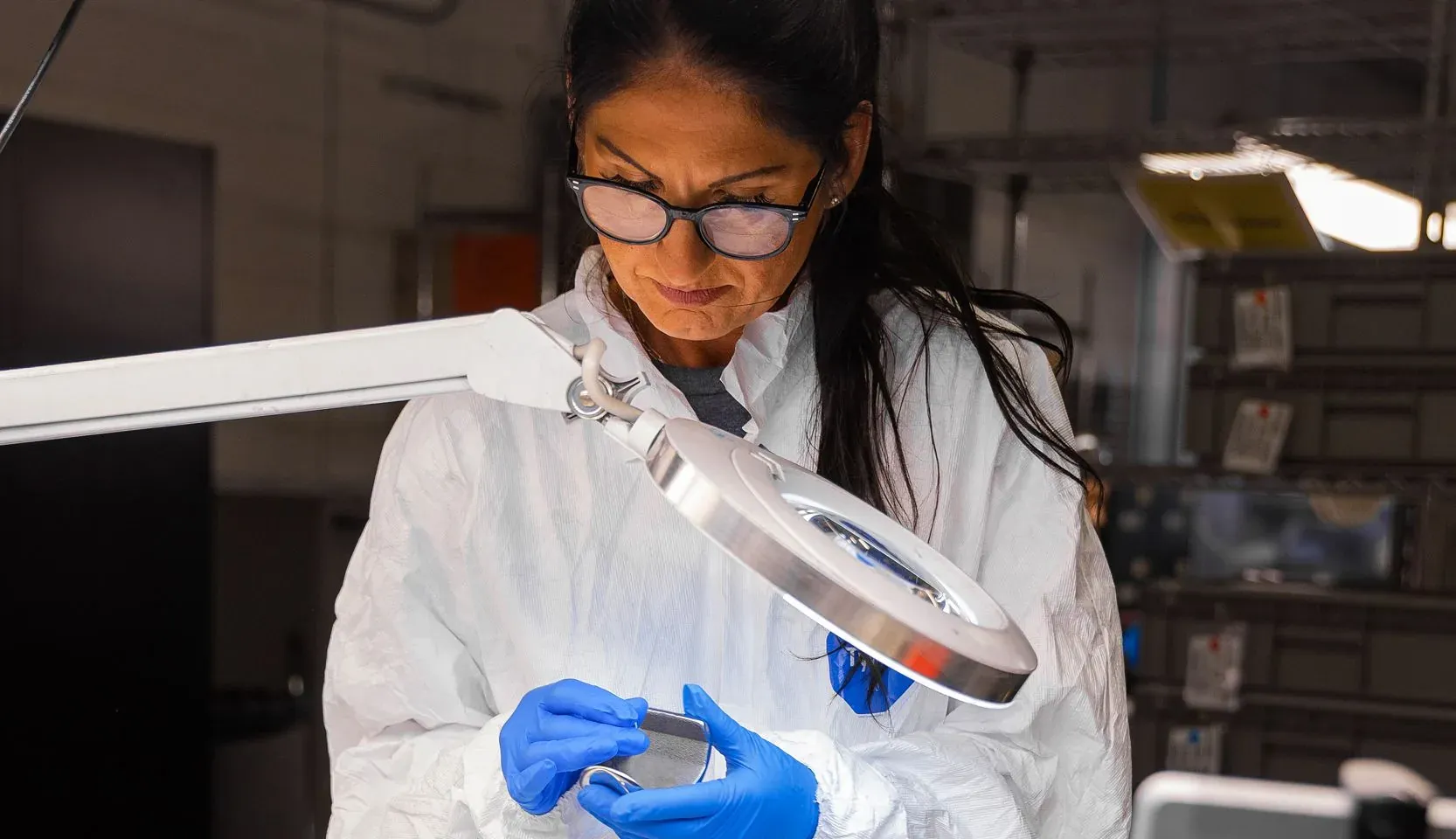 A laboratory technician inspecting a coated coupon under a magnifier