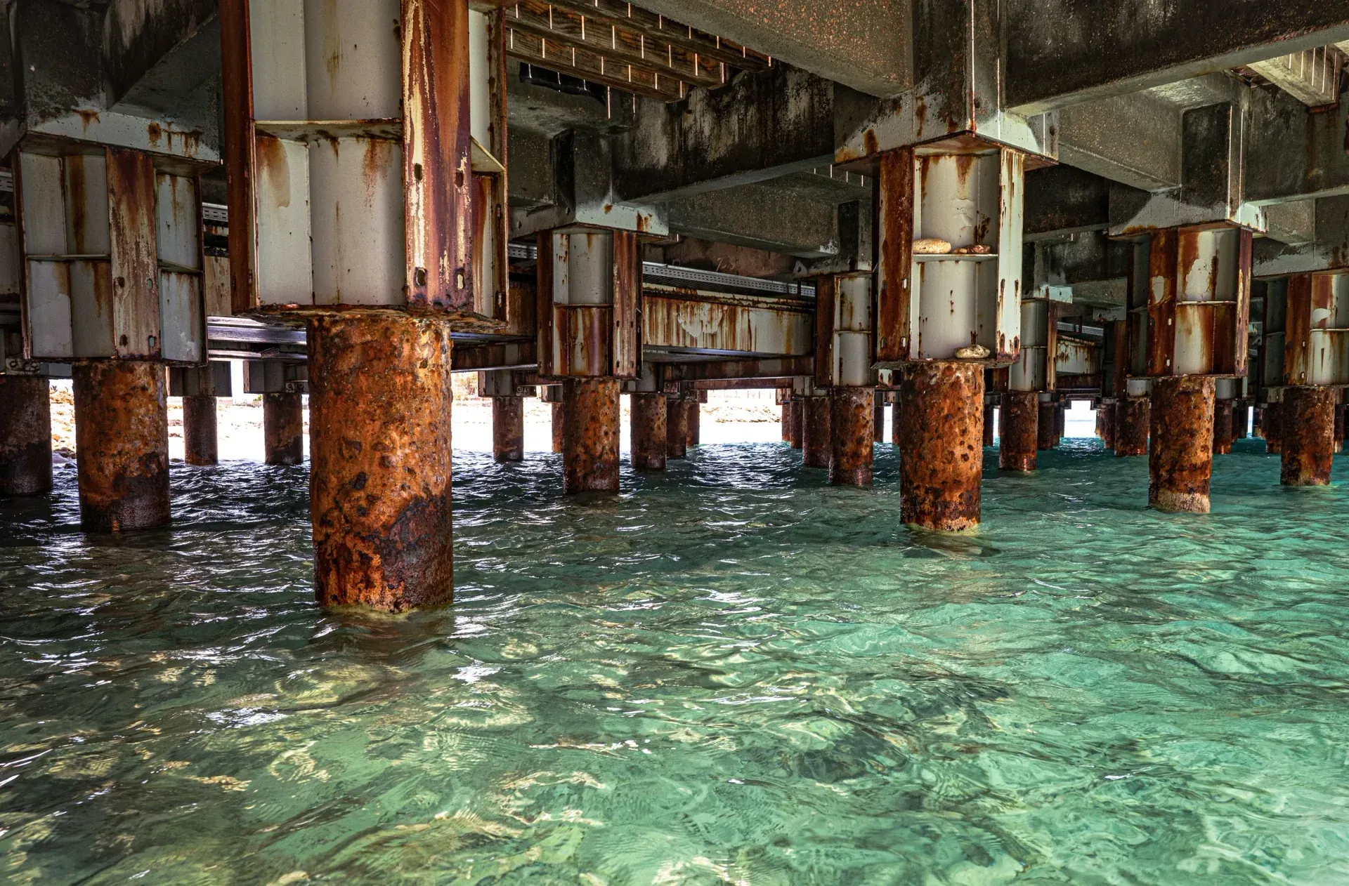 Corroded steel pilings supporting a pier deck above clear shallow seawater