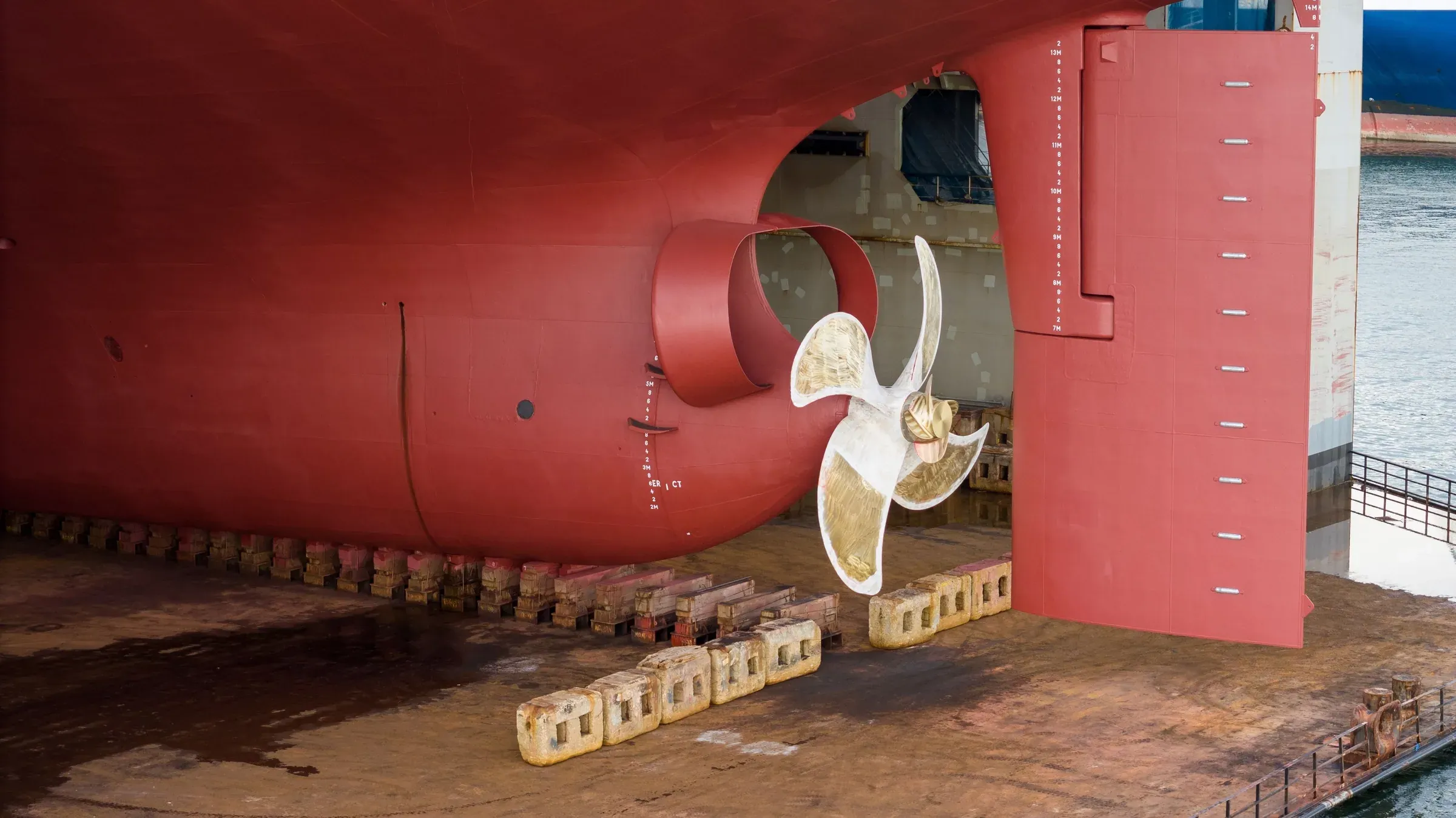 Bronze propeller and rudder of a large ship in dry dock beneath a red antifouling hull