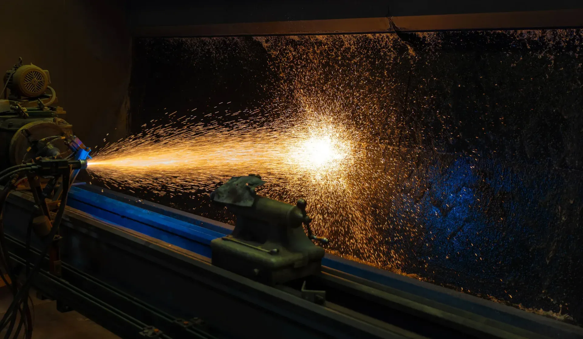 Plasma spray gun laying a coating down a long rotating component in a shower of sparks